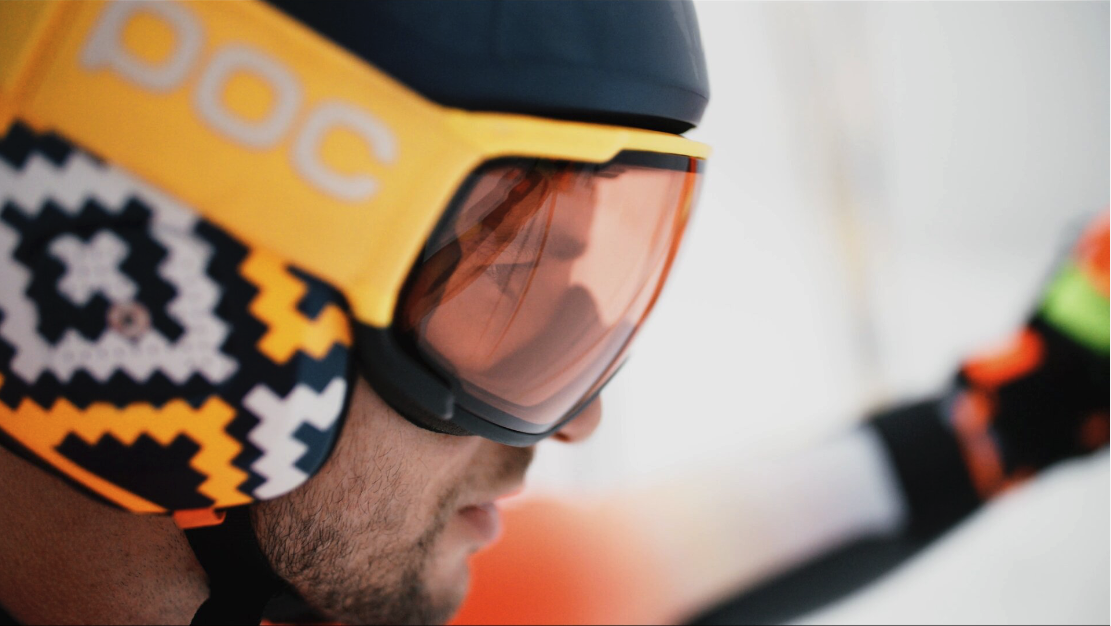 Close-up of a skier wearing a colorful helmet and goggles in a snowy environment.