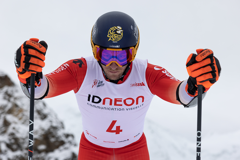 Een skiër in rood-witte uitrusting met El Tony Mate-logo op de helm, klaar voor de race.