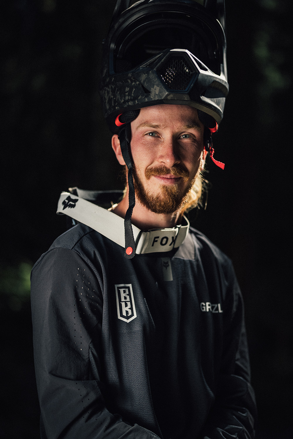 Uomo con casco e abbigliamento sportivo, in posa su sfondo scuro.