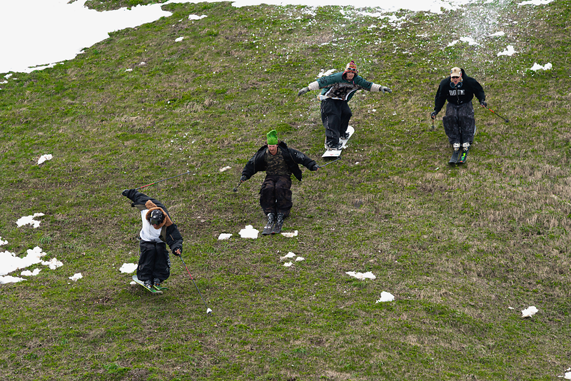 Four people skiing on green grass, surrounded by snow while enjoying El Tony Mate.