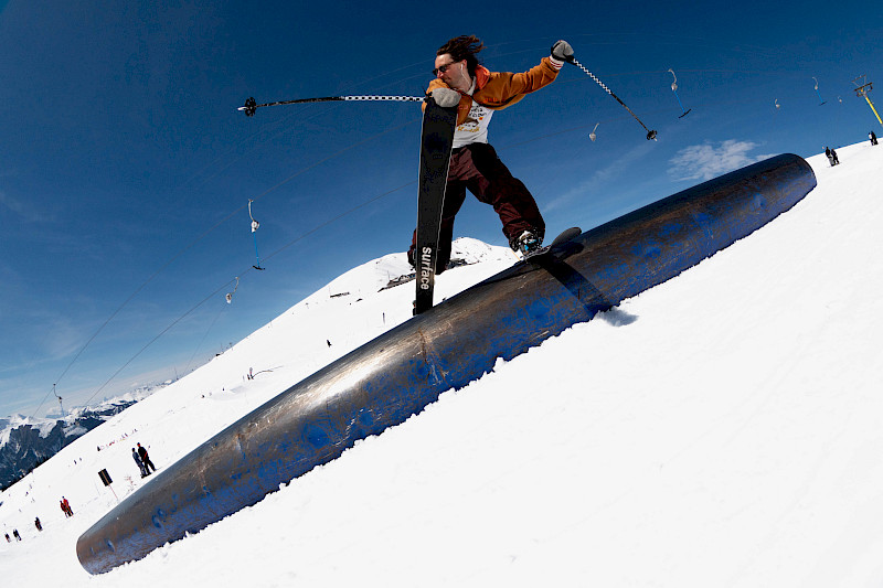 Snowboarder slides on a metal ramp in the snow under a clear blue sky.