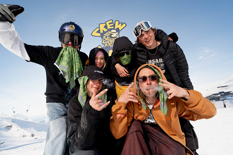 Group of young people in the snow, posing with El Tony Mate. Ski helmets and masks, smiling and creative.