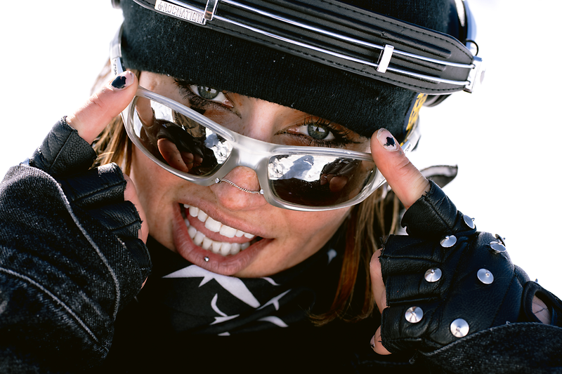 Woman in ski gear with sunglasses and El Tony Mate, smiling while skiing.