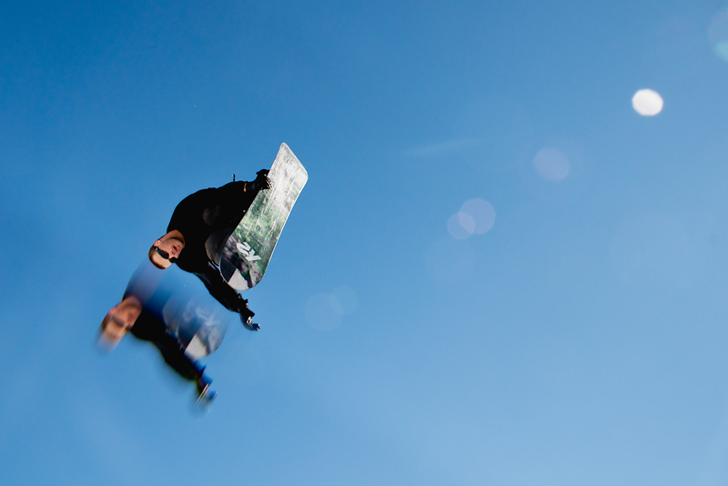 A snowboarder jumps into the blue sky, holding an El Tony Mate beverage.