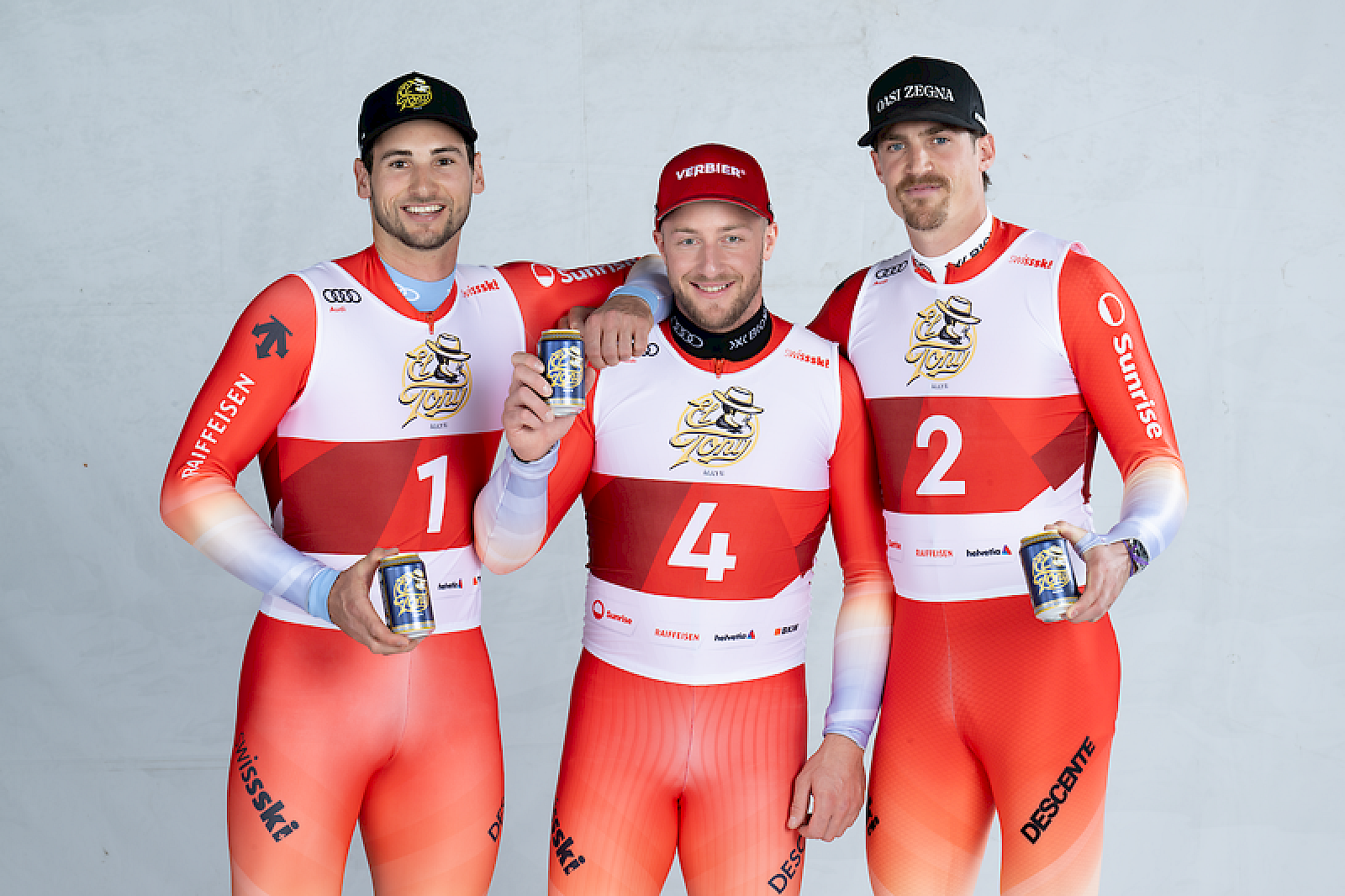 Drei Skisportler in roten Anzügen halten El Tony Mate Dosen in der Hand.