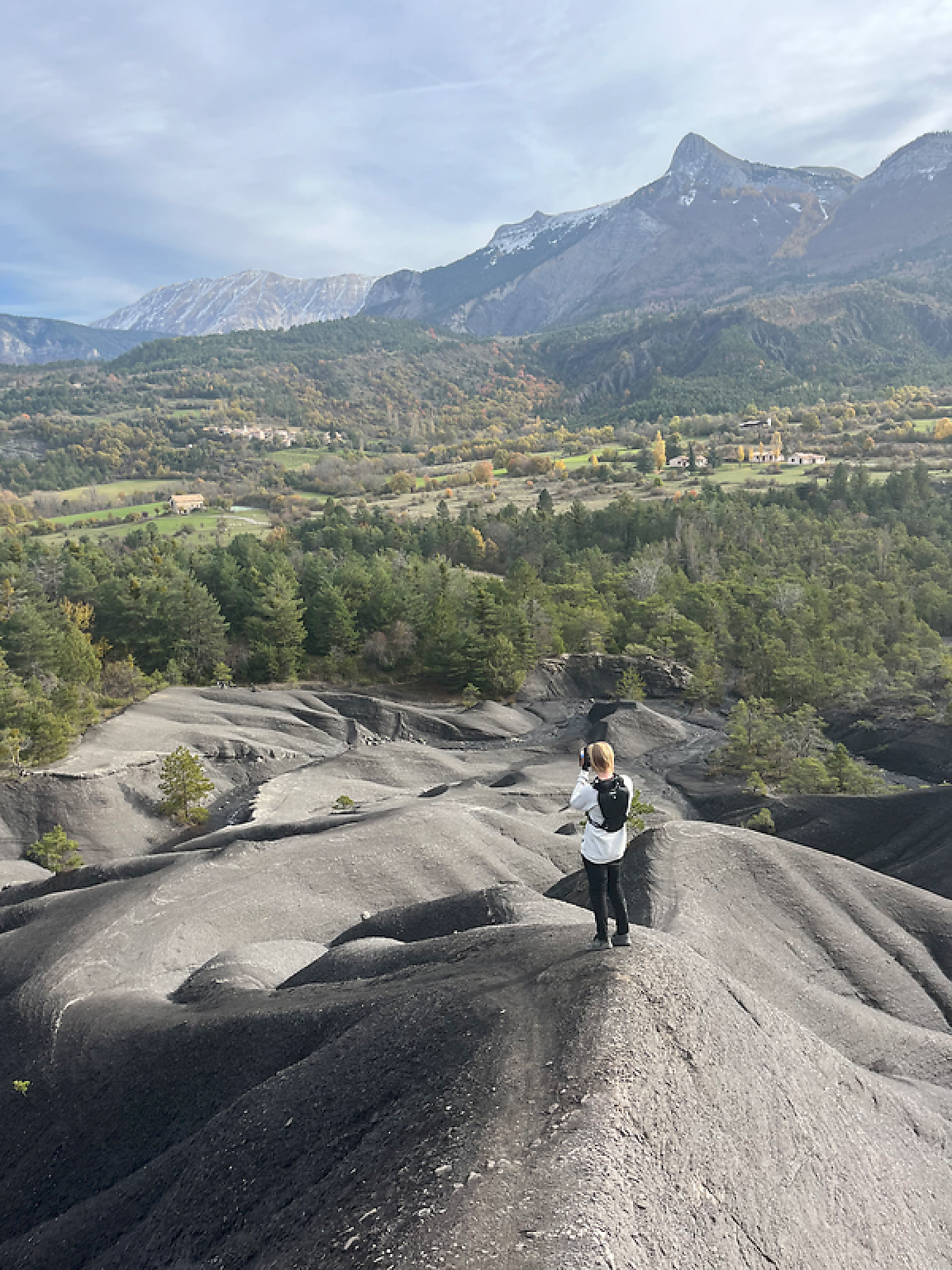 Un visitatore è in piedi su un terreno nero con montagne sullo sfondo, godendo il paesaggio.
