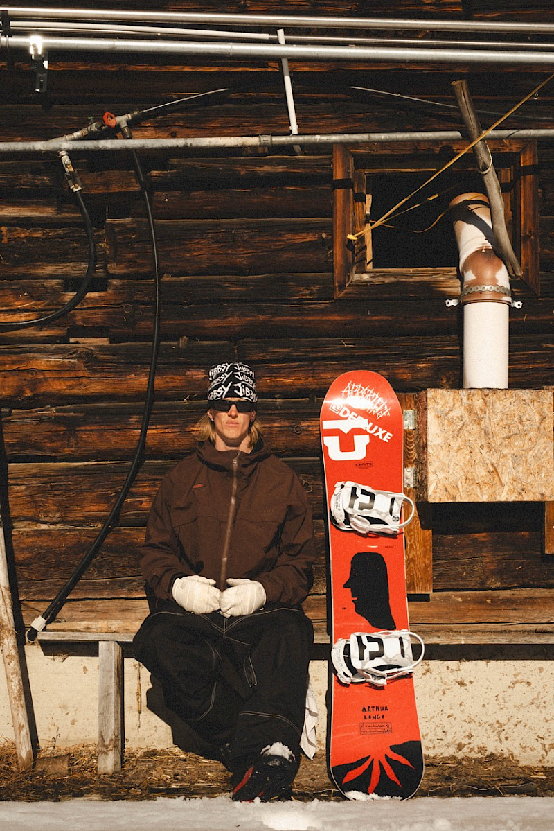Gustaf Lundstrom sits on a bench in front of a cabin, ready for a snowy adventure.