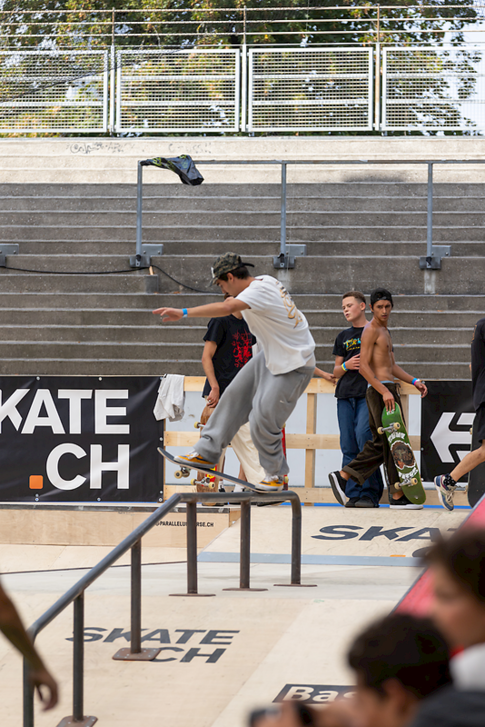 Ein Skater führt einen Grind an einer Metallstange in einer Skatepark-Umgebung aus.