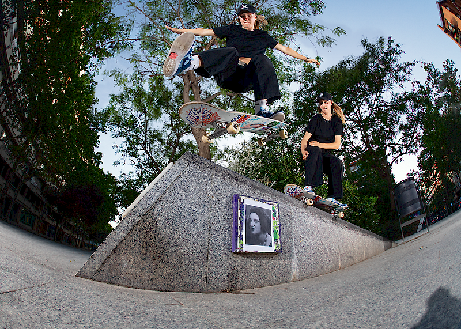 Skateboarder salta sopra un'opera d'arte su un blocco, circondato da alberi.