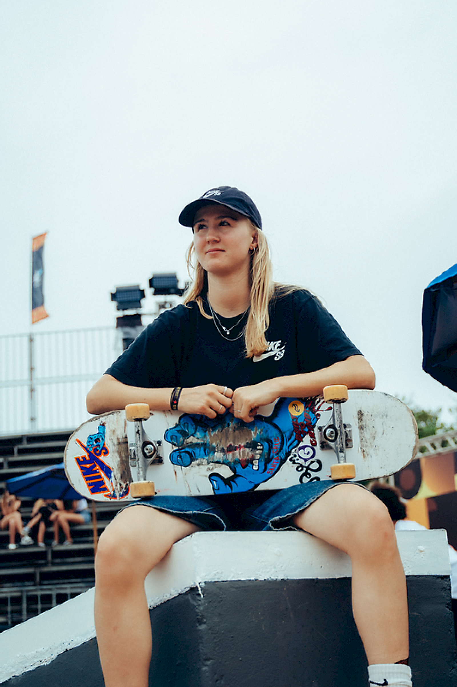 Skateboarder seduta con la sua tavola, osservando l'azione durante un evento all'aperto.