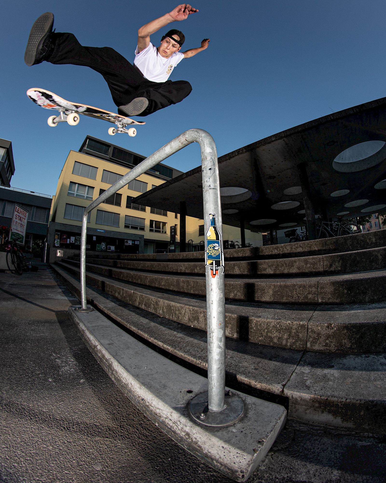 Skater salta sopra un corrimano in un ambiente urbano, bevanda El Tony Mate nelle vicinanze.