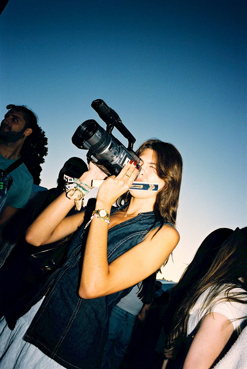 A woman holding a camera and drink at an outdoor event.