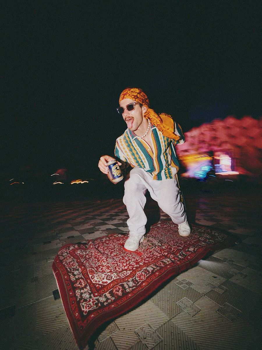 Man in colorful clothing enjoys El Tony Mate on a carpet at an event.