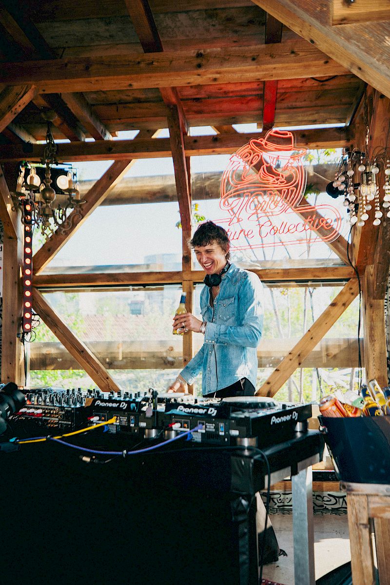 DJ che gusta una bevanda El Tony Mate in un ambiente rustico pieno di luci.