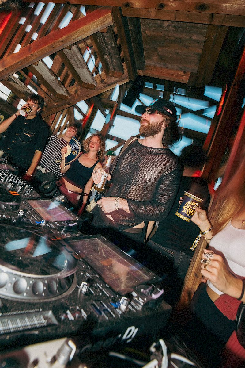 Persone che festeggia in una location rustica con bevande e attrezzature DJ.