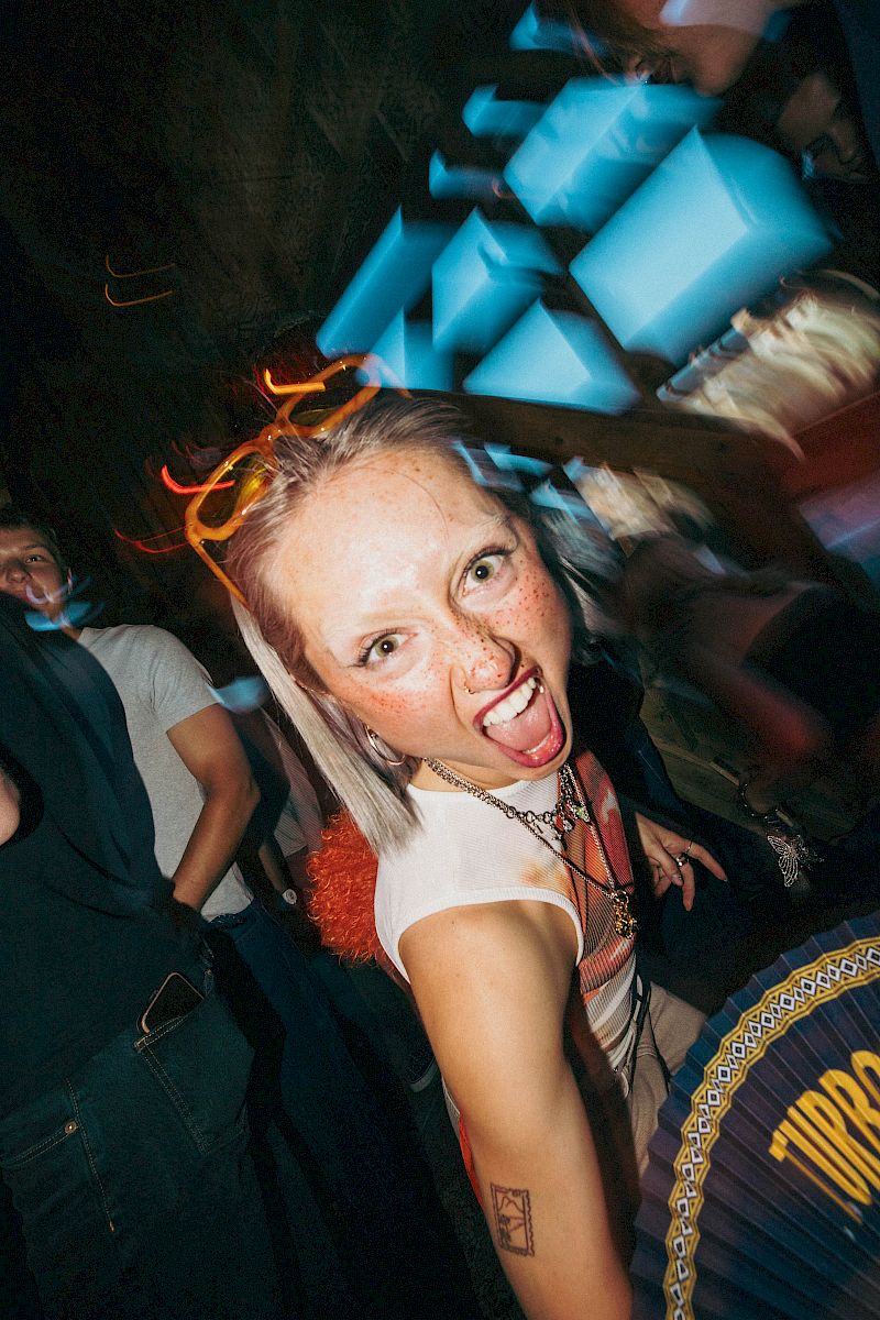 Persona entusiasta in un'atmosfera da festa con luci vivaci e bevanda El Tony Mate.