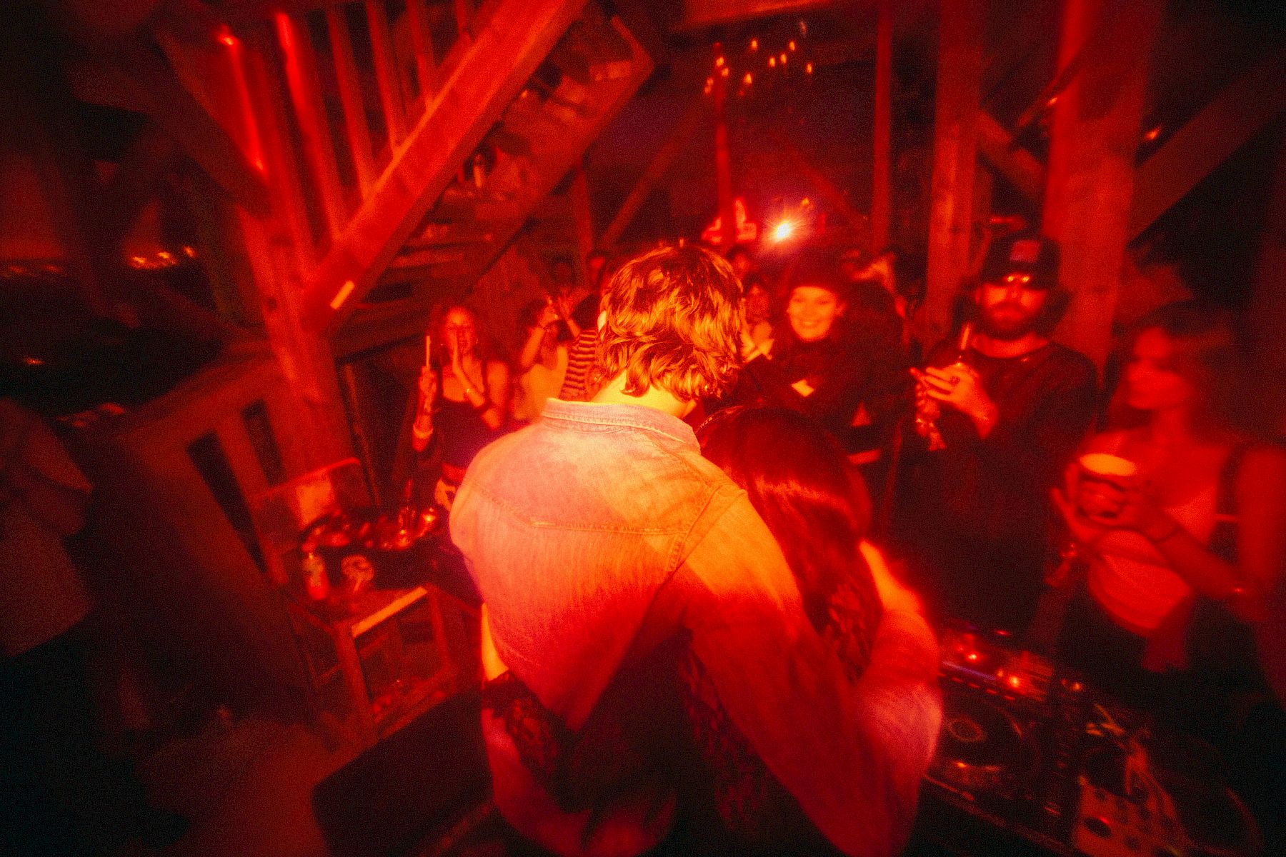 Una coppia si abbraccia a una festa, circondata da persone felici e da luci rosse.