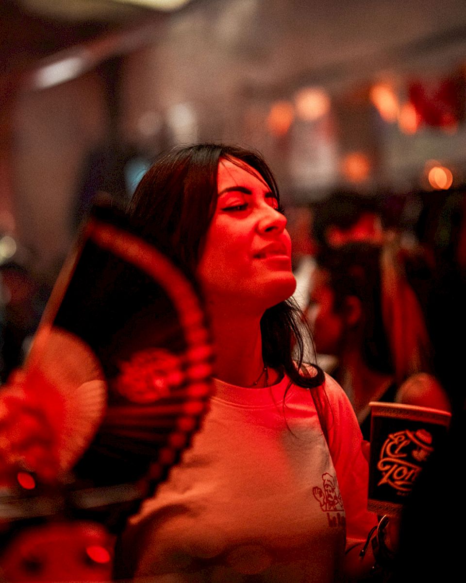 Vrouw met een waaier en drank in een levendige, feestelijke sfeer.