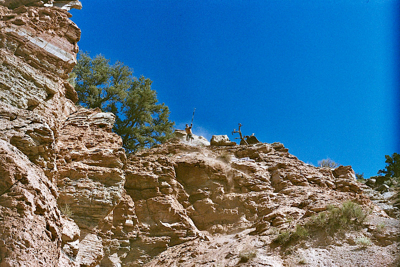 Un avventuriero salta da una roccia gustando El Tony Mate, con il cielo sullo sfondo.