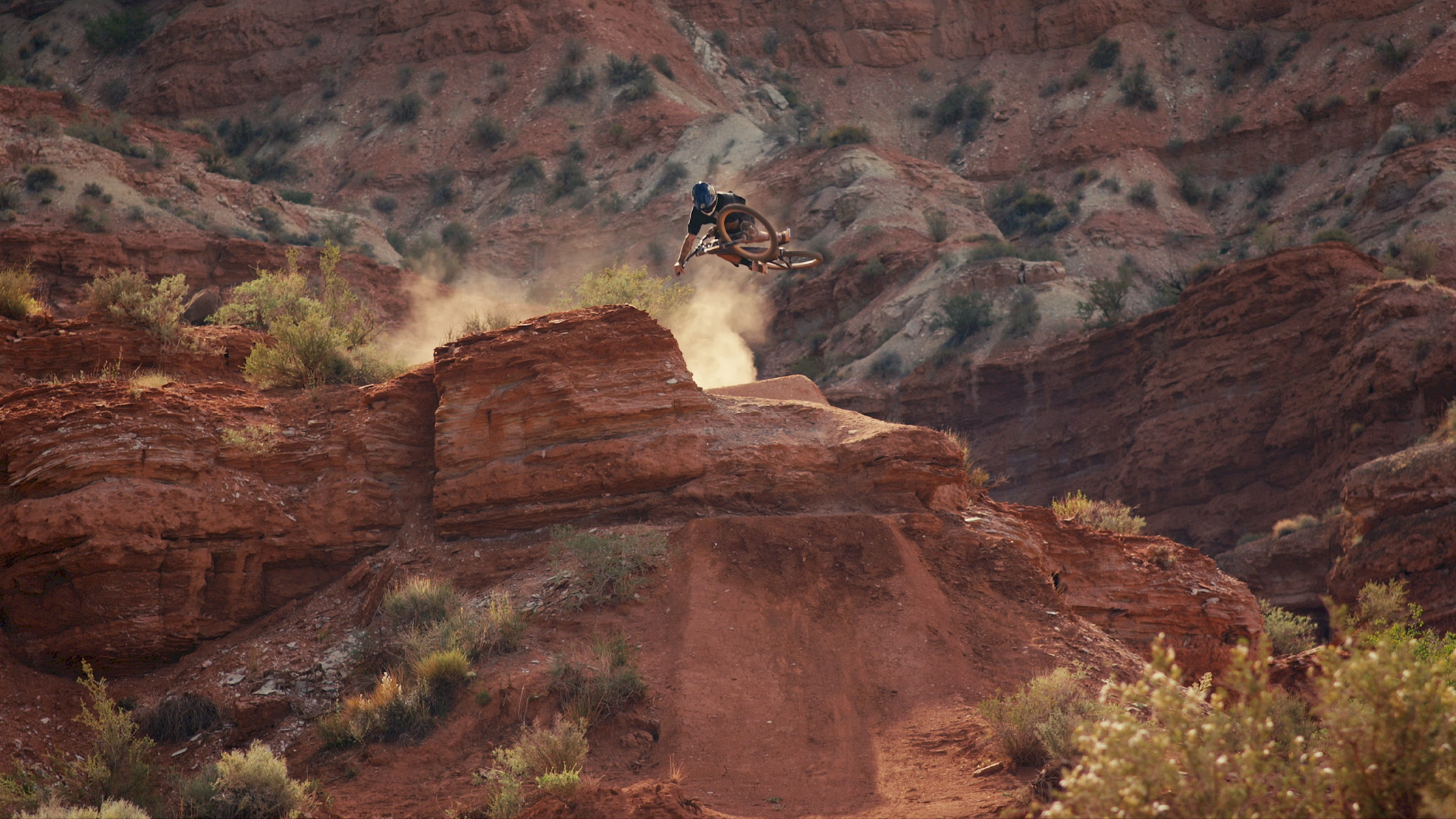 Un ciclista di mountain bike salta da una scogliera in un paesaggio di rocce rosse.