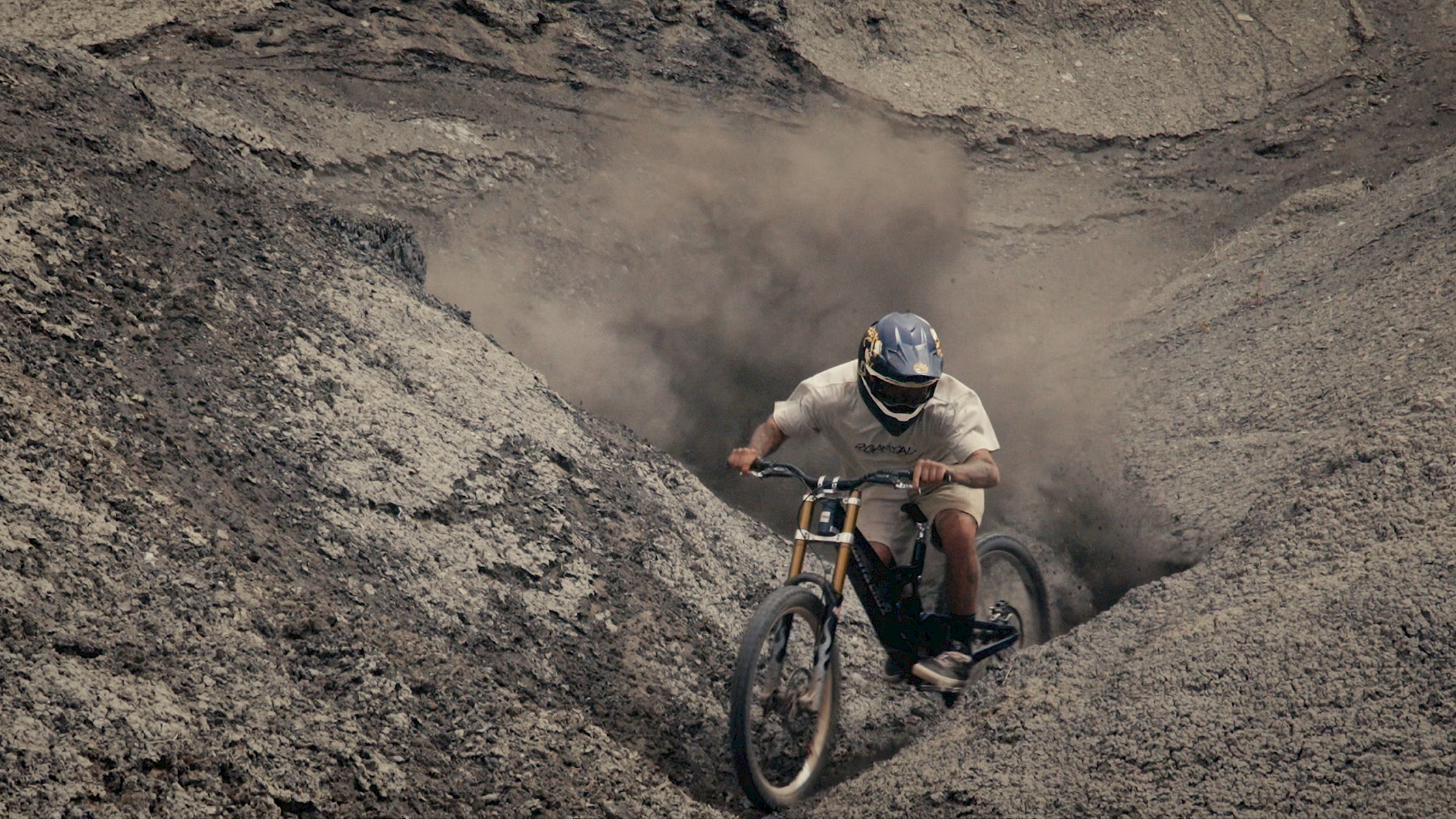 Un biker su una mountain bike attraversa una fossa polverosa, creando una nuvola di polvere.