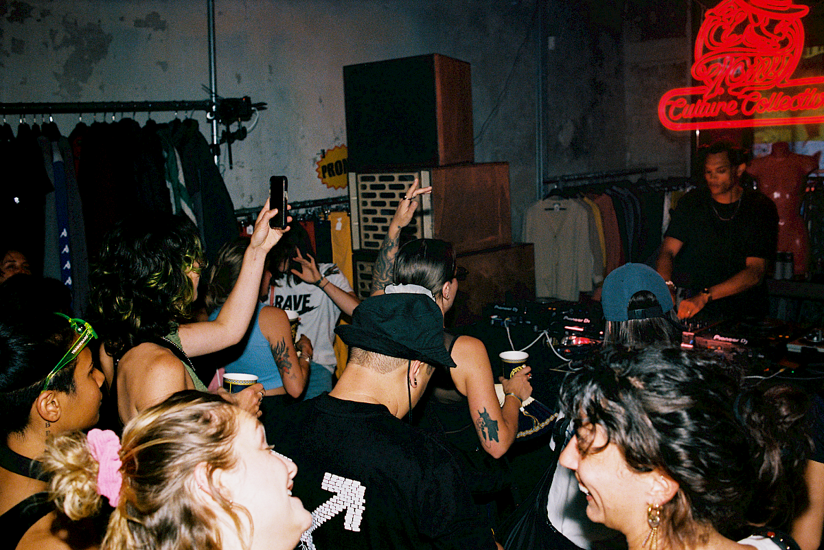 Crowd enjoying music at a store with DJ while sipping El Tony Mate beverages.