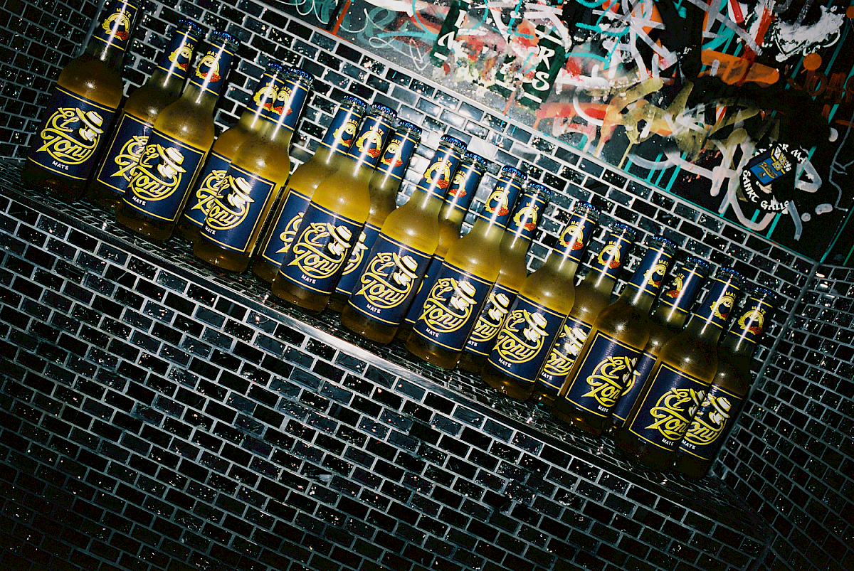 Row of El Tony Mate bottles against a graffiti-covered wall.