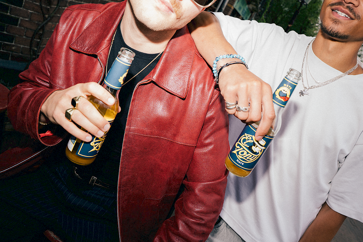 Two people holding El Tony Mate bottles in a trendy setting.
