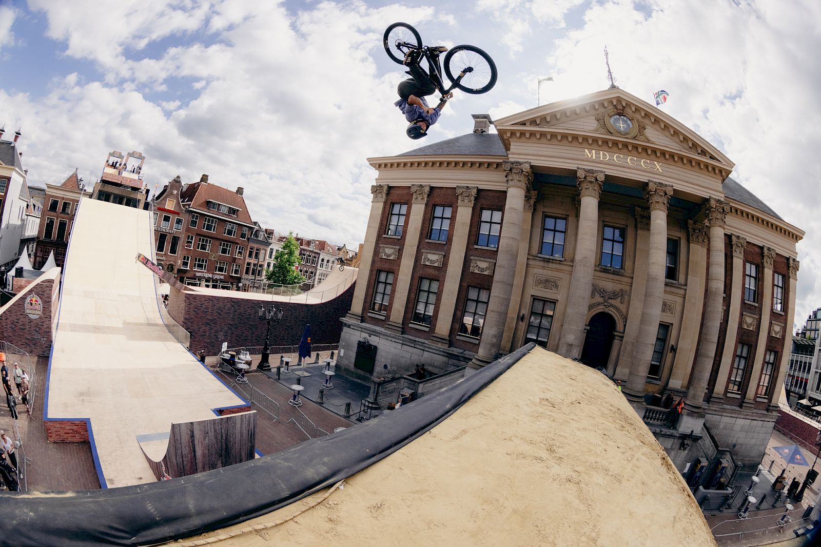 Un ciclista BMX esegue un trucco su una rampa davanti a un edificio storico ad Amsterdam.