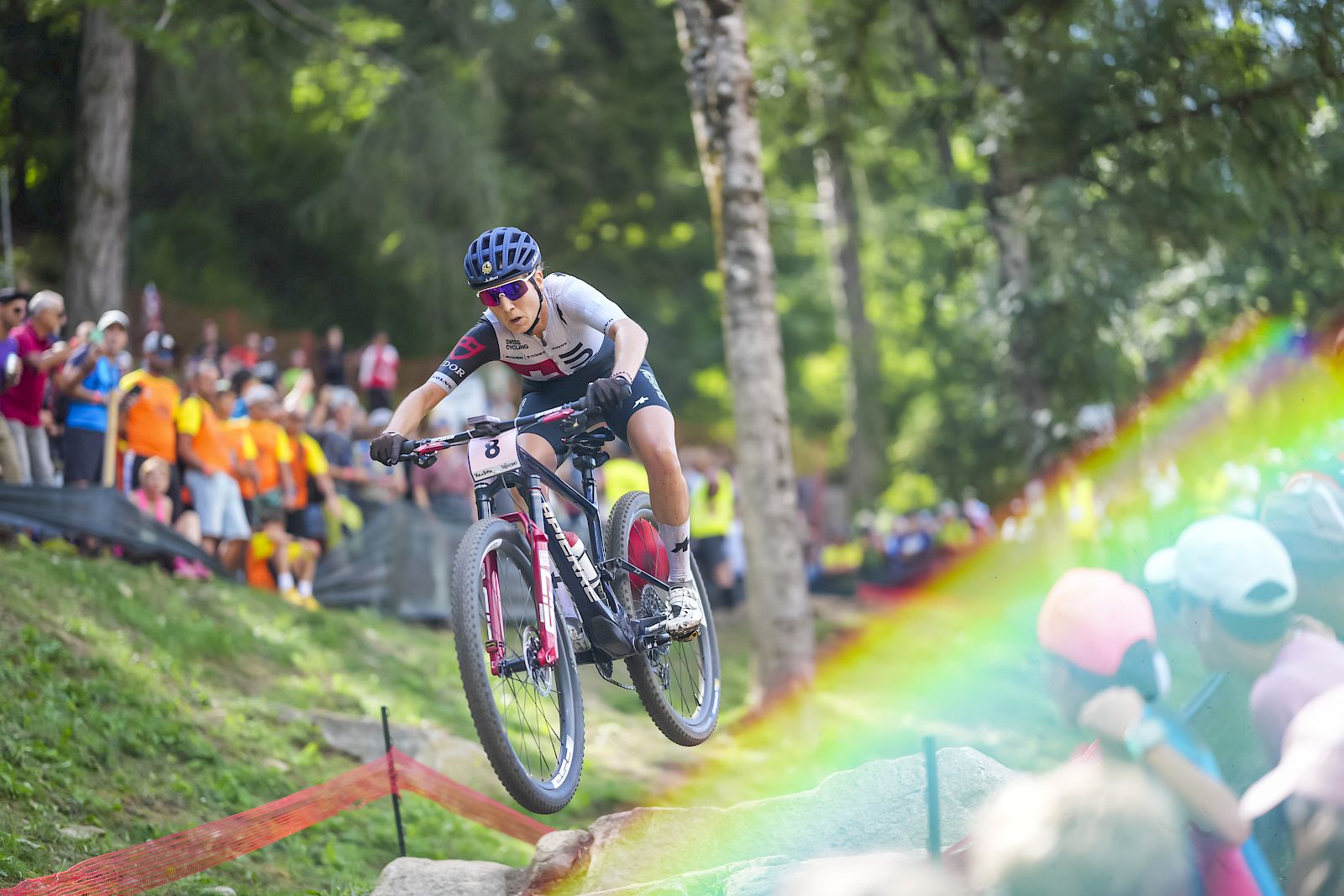 Een mountainbiker springt over rotsen, omringd door juichende toeschouwers en levendige kleuren.