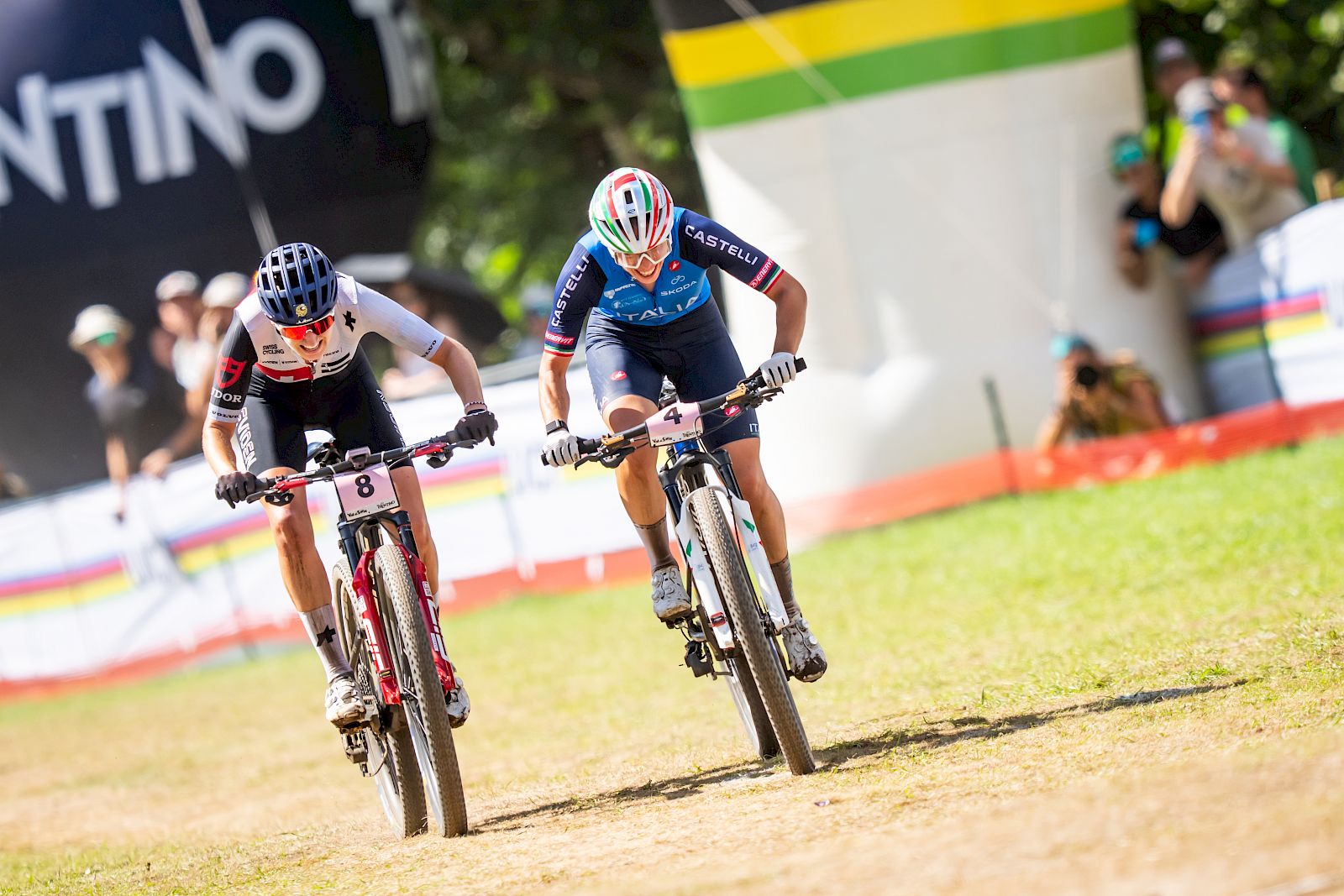 Twee fietsers strijden om de eerste plaats in een mountainbikerace met El Tony Mate drankje op de achtergrond.